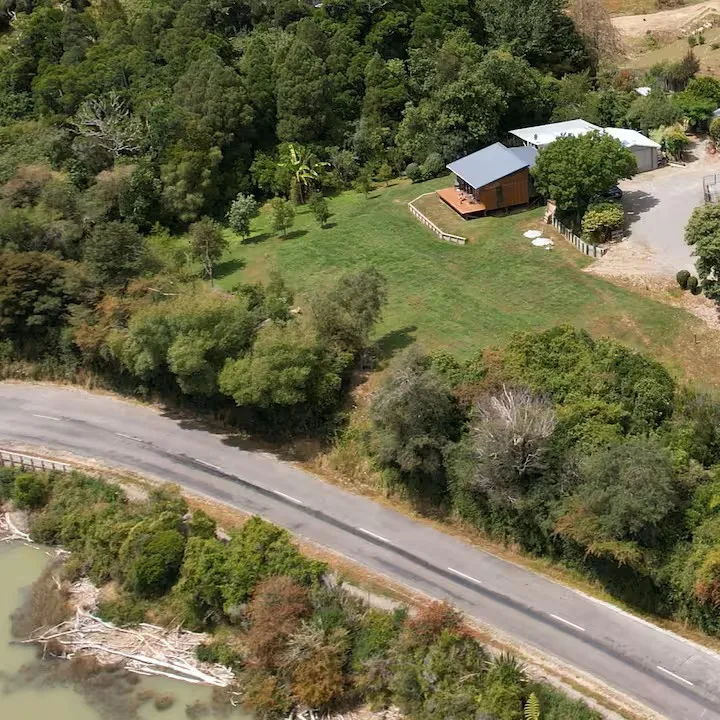 Aerial view of The Milestone cabin in a green clearing beside the water