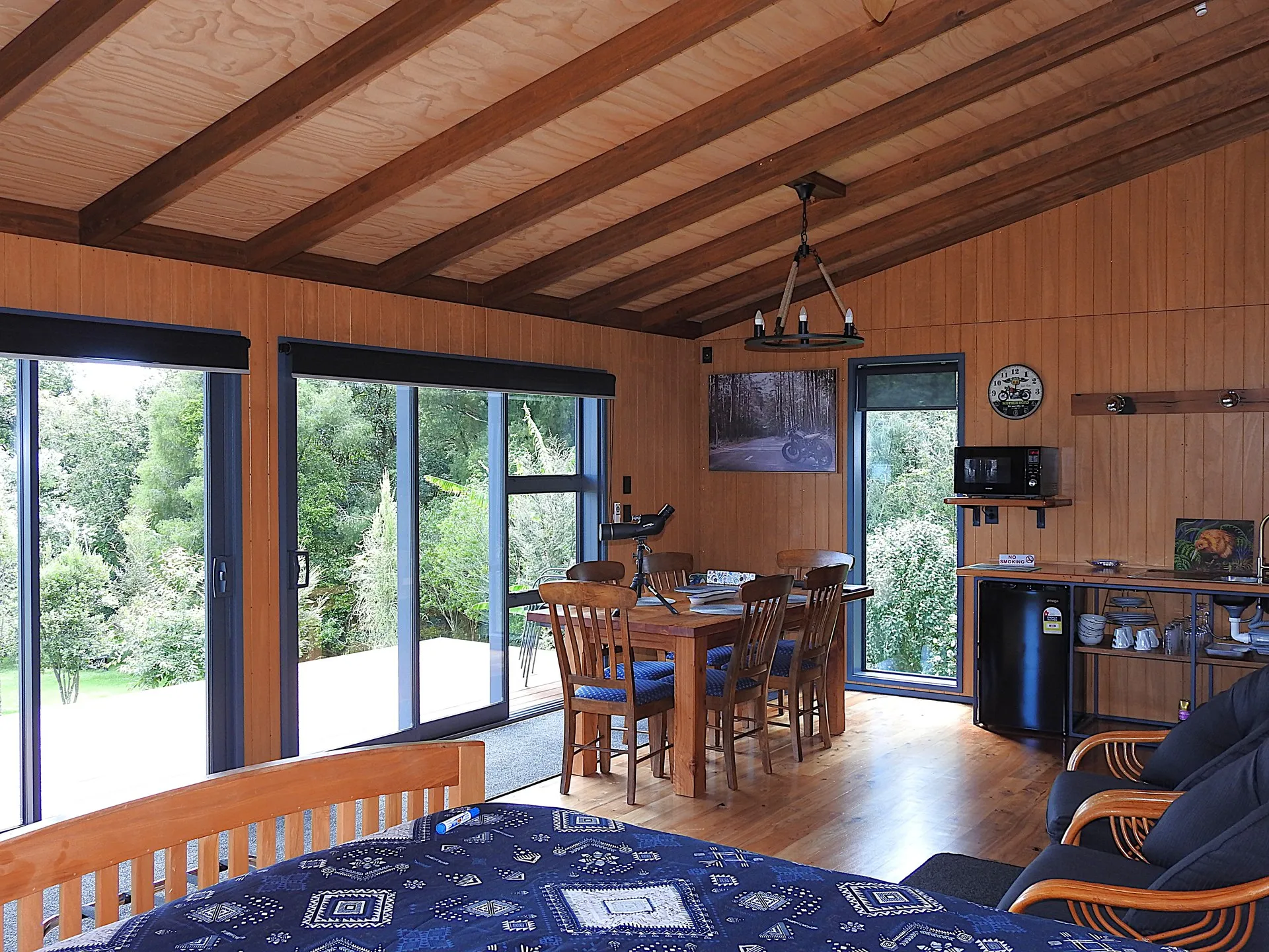 The warm timber interior — bed, lounge and kitchenette, with sliding glass doors to the bush