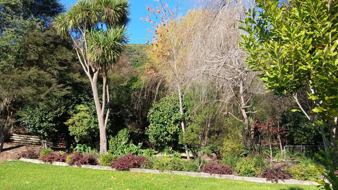 Established garden beds and lawn at The Milestone, native bush and autumn colour behind