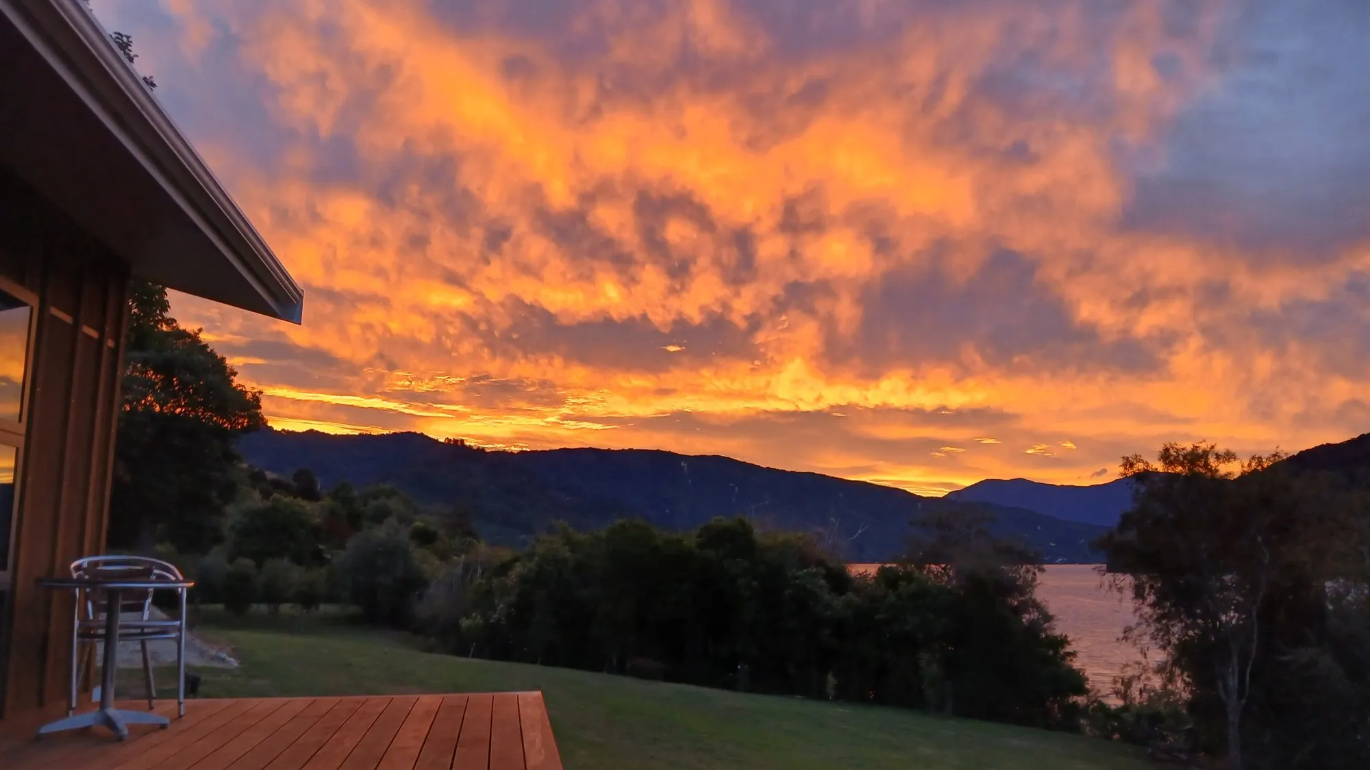 A blazing gold-and-orange sunset over the water of the Sounds, seen across the cabin’s timber deck