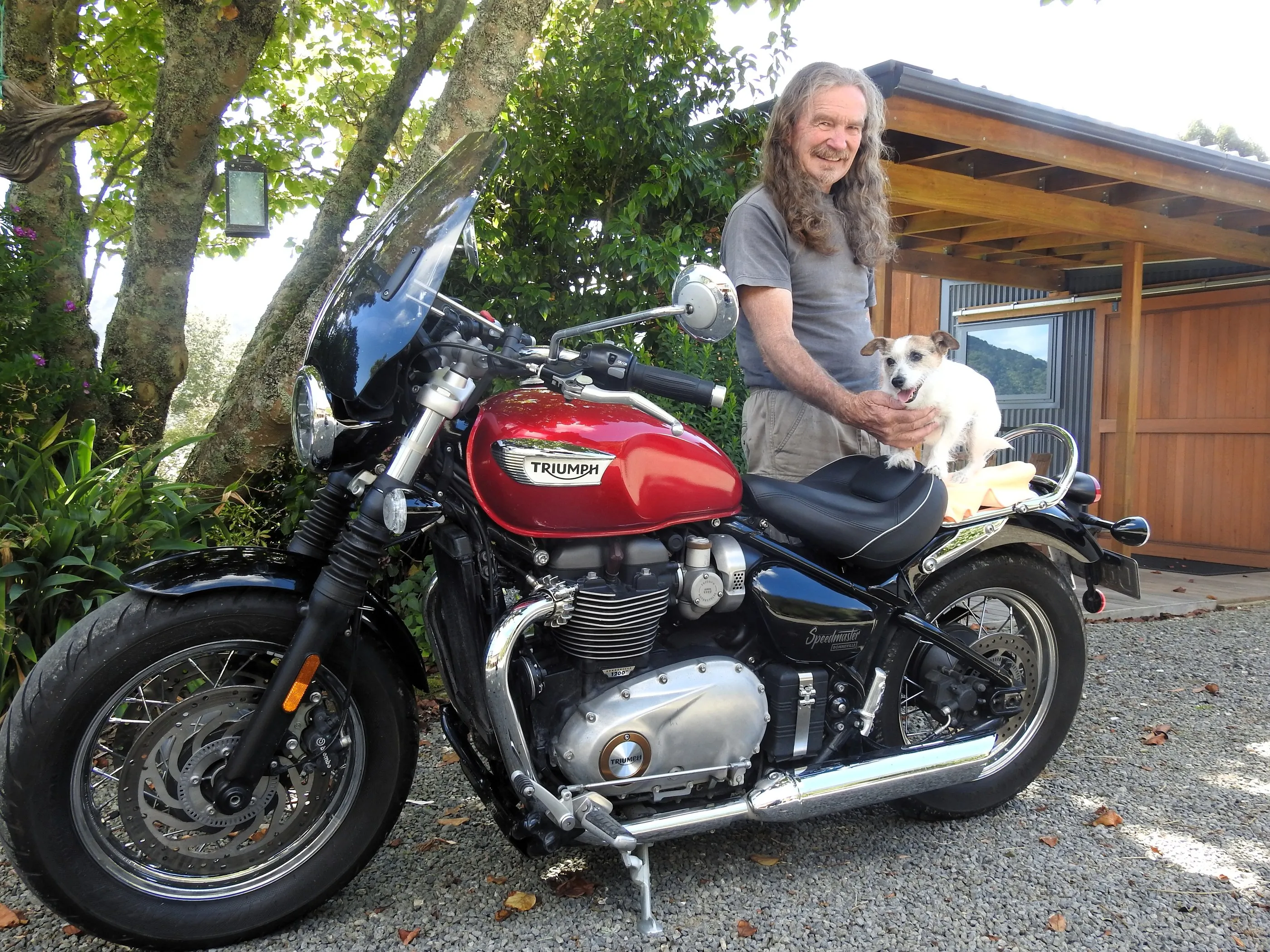 Lionel, the owner, with his Jack Russell beside his Triumph motorcycle, the cabin behind
