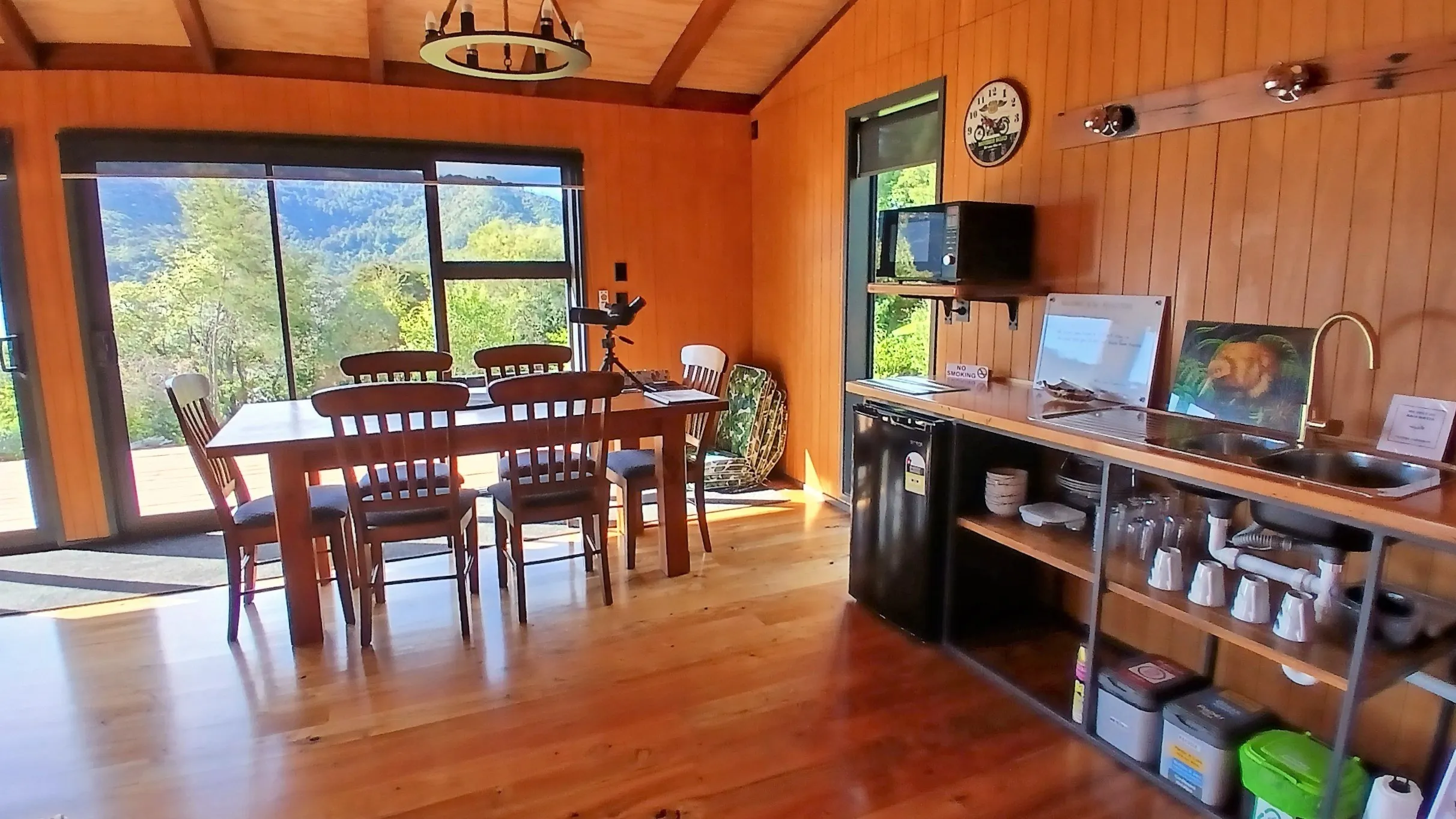 The dining table and kitchenette in warm afternoon light, a spotting scope at the window